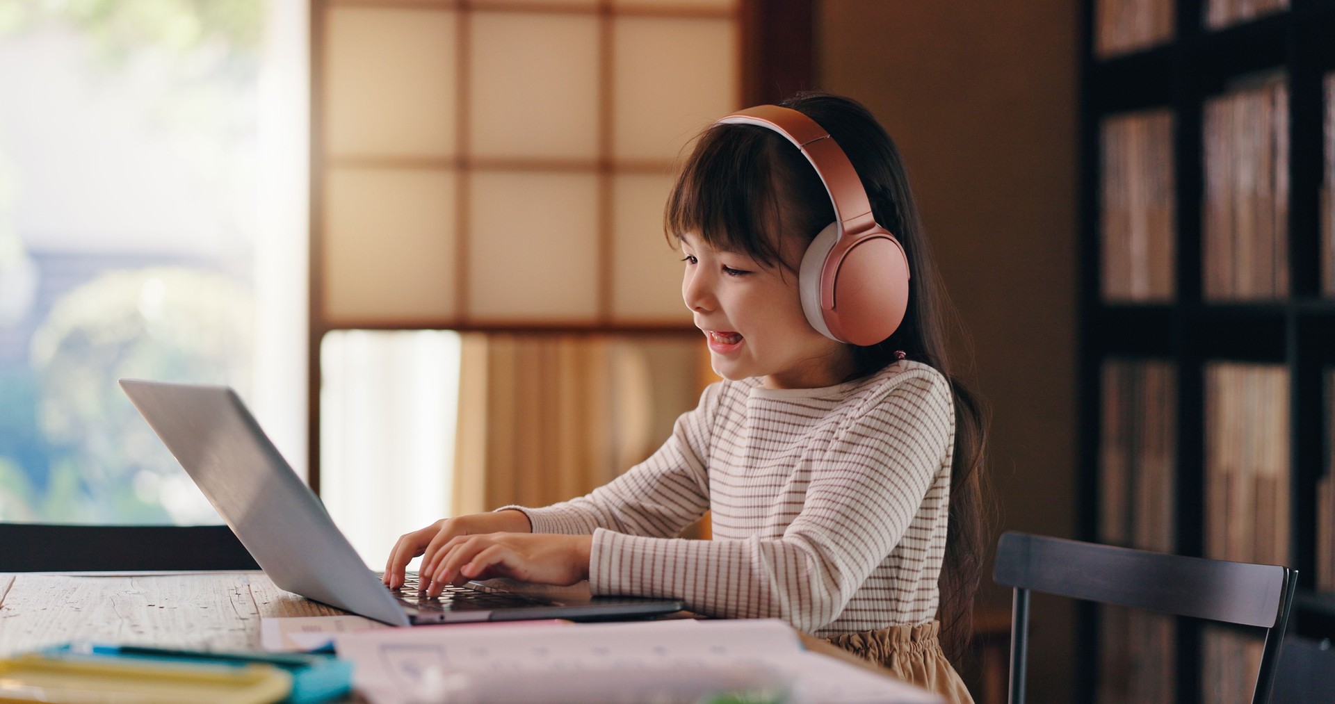 Elearning, studying and child with laptop, headphones and education for girl, listening or typing. Home, happy and online and practice for exam, audio and podcast for knowledge, smile or kid in Japan